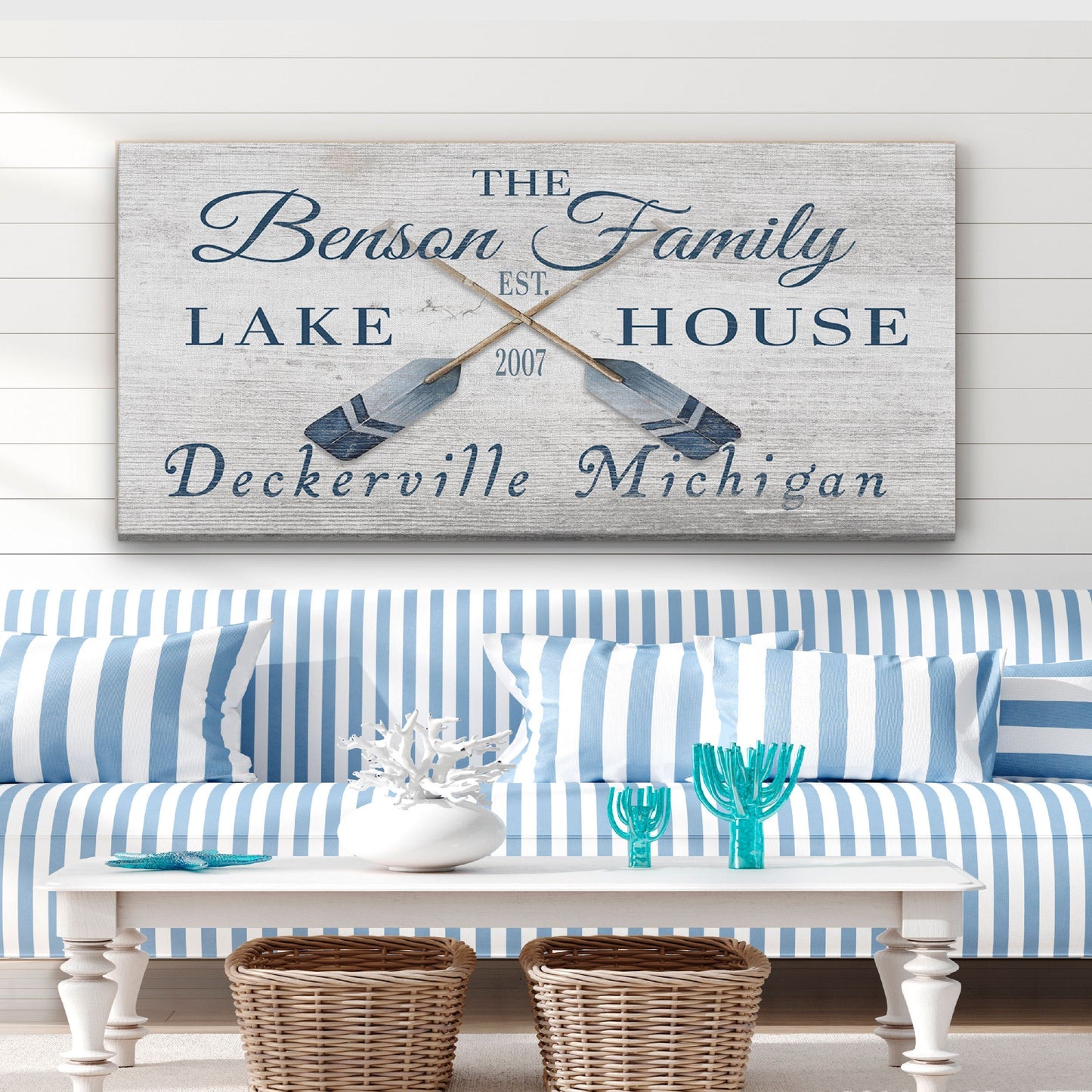 Decorative sign with 'The Benson Family Lake House' on a wall above a blue and white striped sofa.