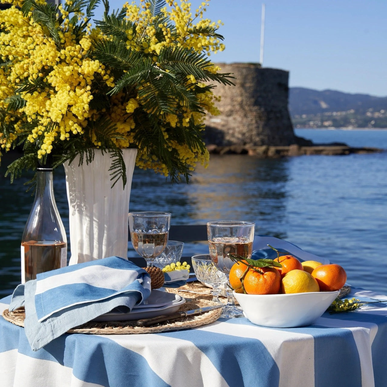 Table setting with fruit and drinks by a body of water with a castle in the background