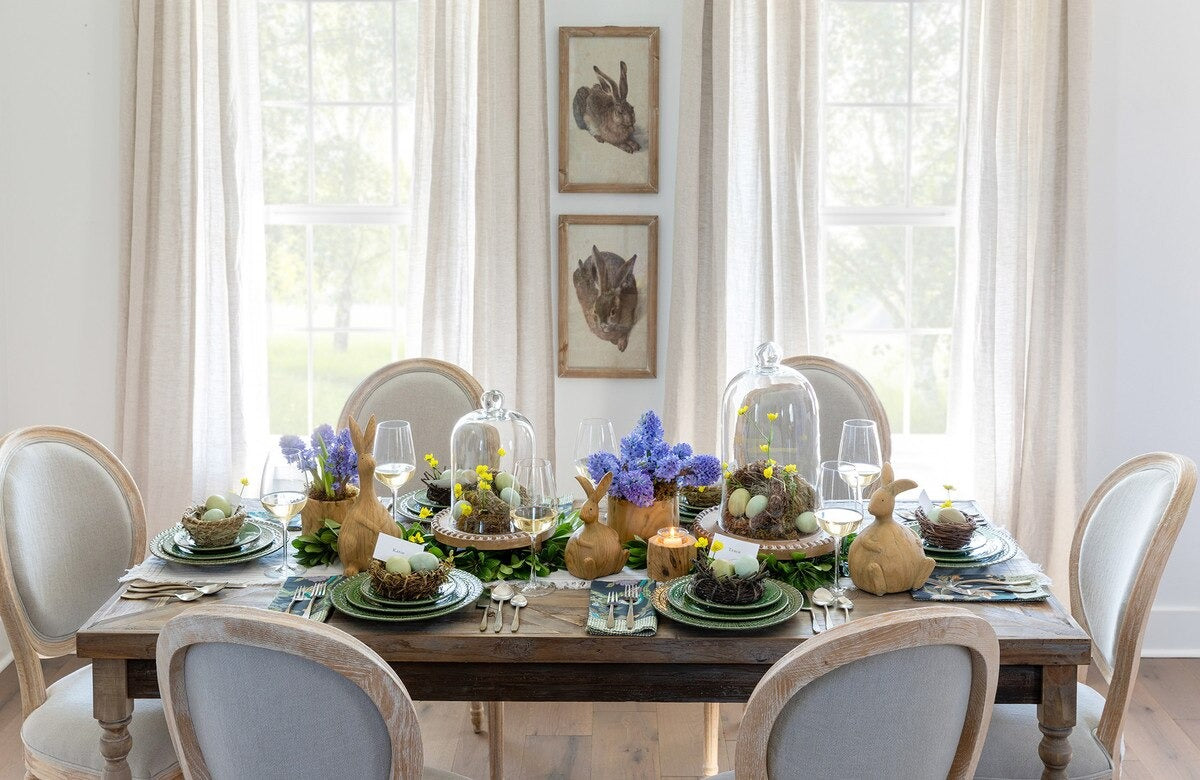 Dining room table set for Easter with decorative eggs and flowers, surrounded by chairs.