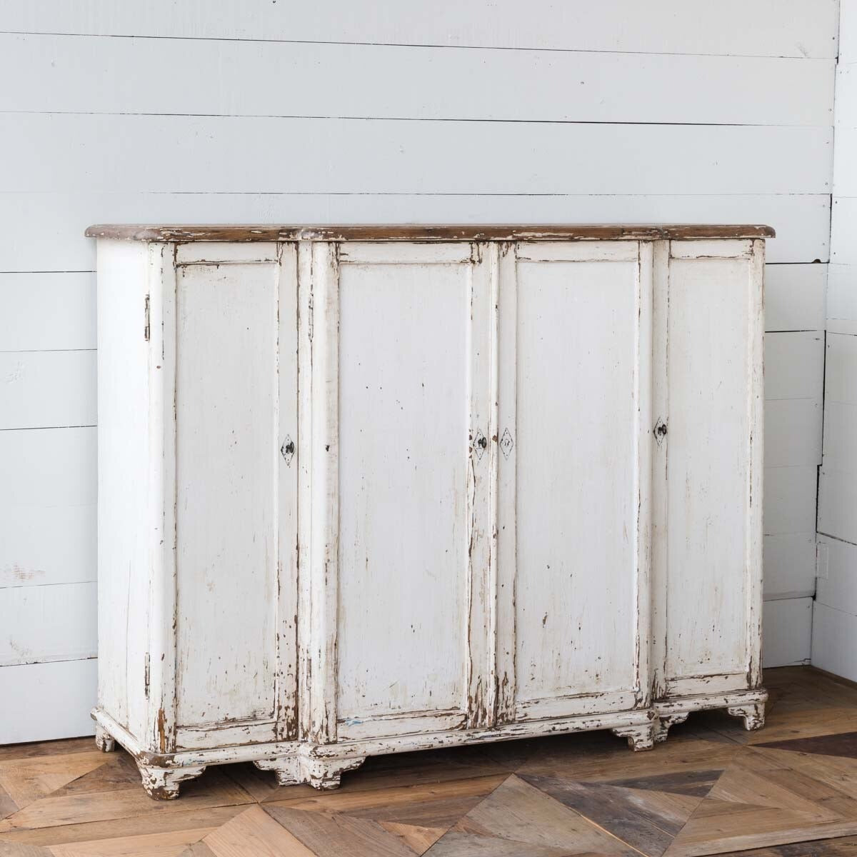 Vintage-style white cabinet with chipped paint on a wooden floor and light gray wall.