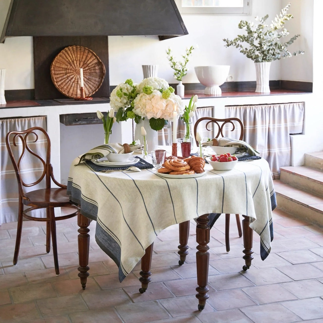 Dining table set with a white tablecloth, plates, and flowers in a kitchen.