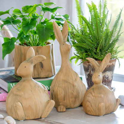 Three wooden rabbit sculptures on a surface with plants in the background