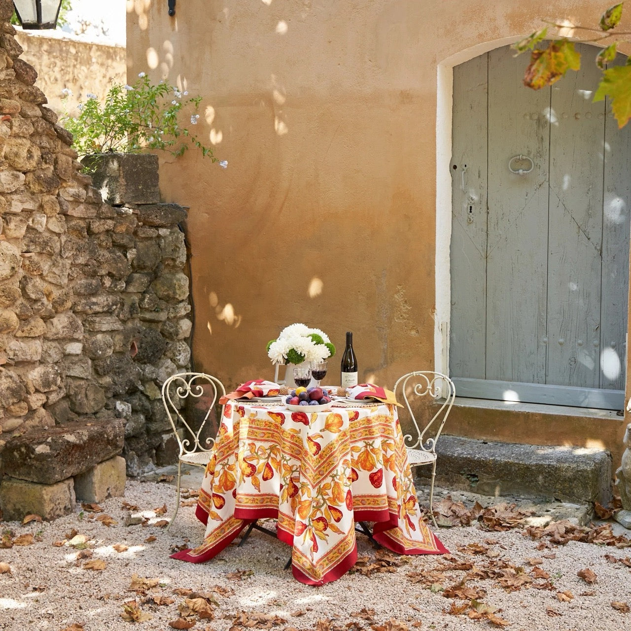 Outdoor setting with a table set for a meal against a stone wall and door.