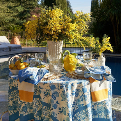 Outdoor table setting with yellow flowers, lemons, and a blue floral tablecloth.