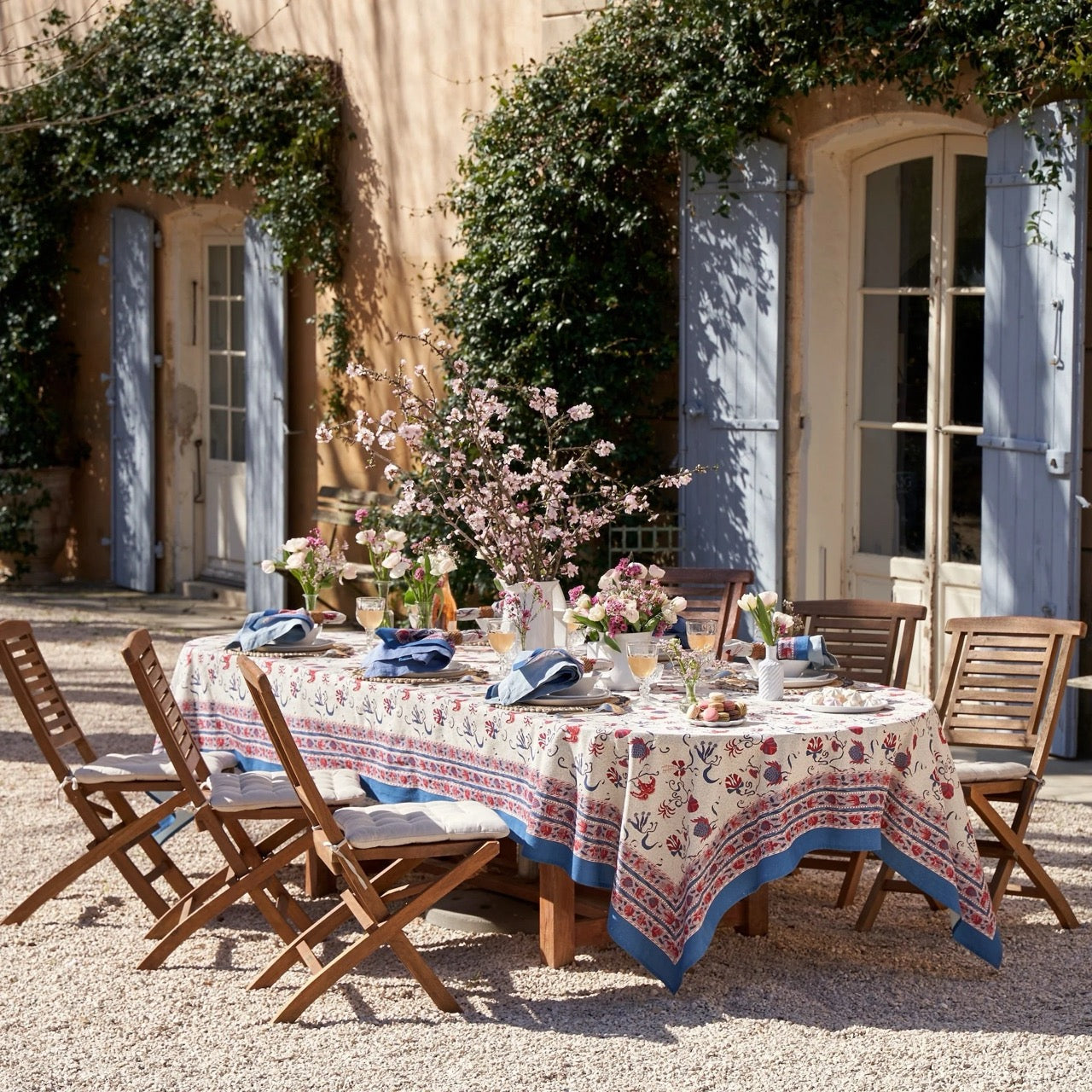 Outdoor dining setup with a floral tablecloth and chairs in front of a building with blue shutters.