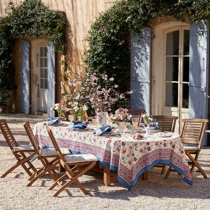 Outdoor dining setup with a floral tablecloth and chairs in front of a building with blue shutters.