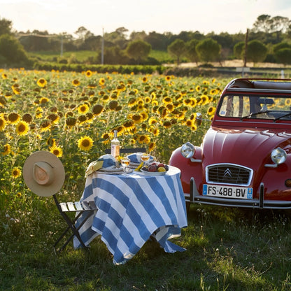 Red vintage car parked in a sunflower field with a table set for a meal.