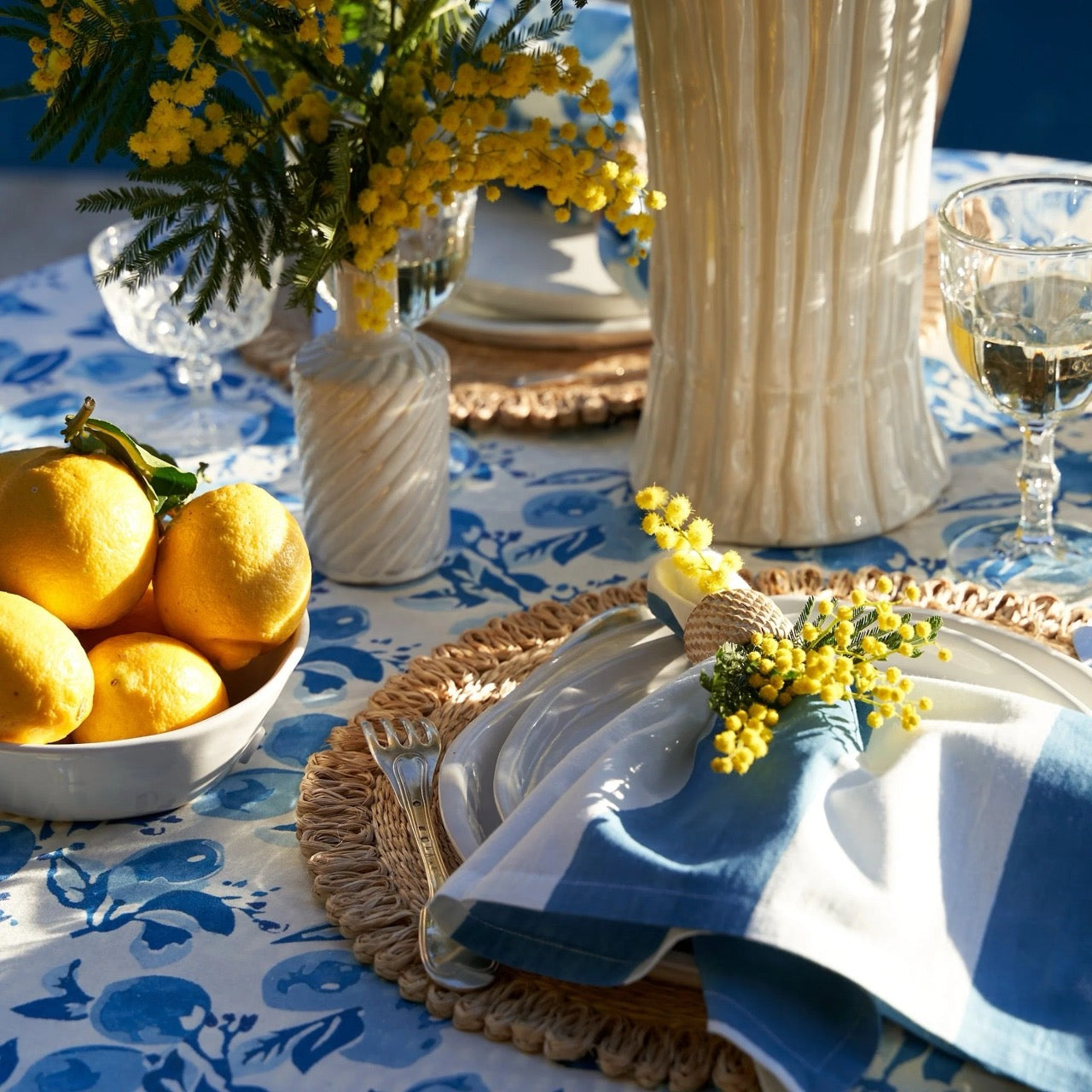 Table setting with lemons, flowers, and cutlery on a blue floral tablecloth.