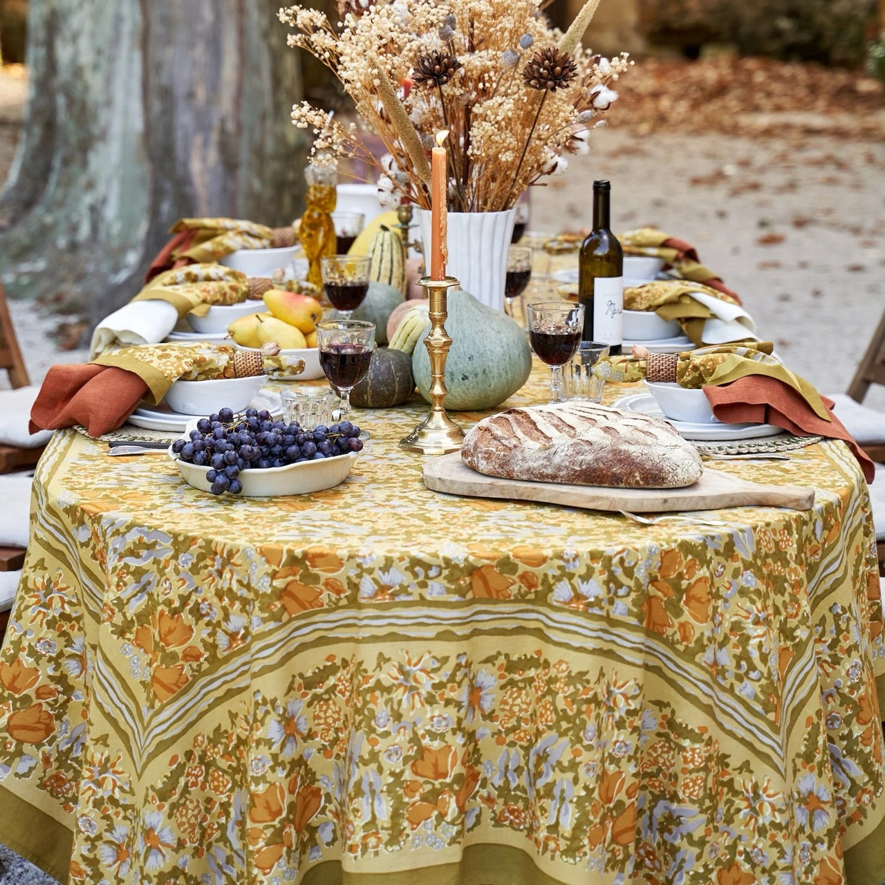 Outdoor table setting with a floral tablecloth, bread, wine, and fruit.