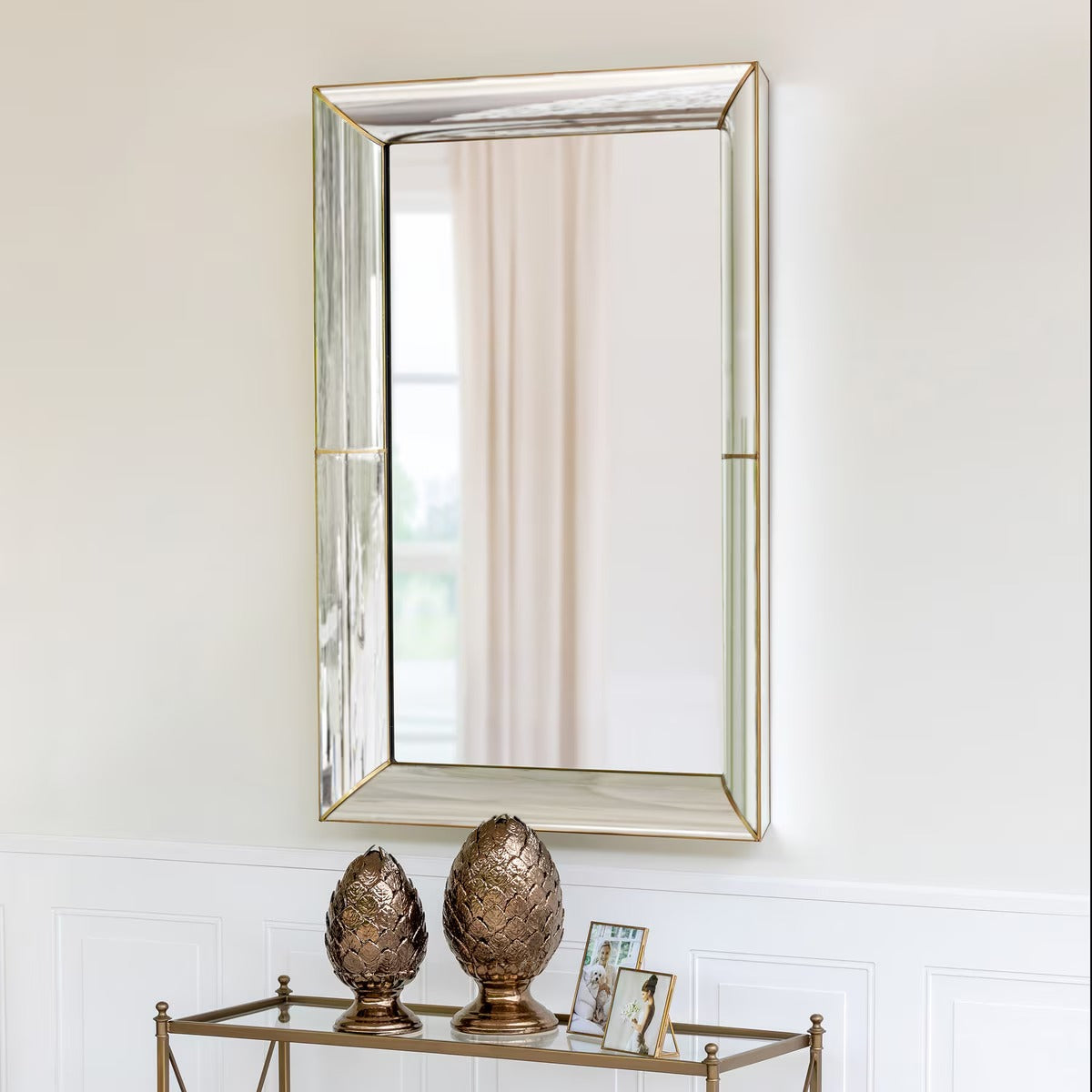 Decorative mirror with gold frame on a white wall above a glass table with decorative items.
