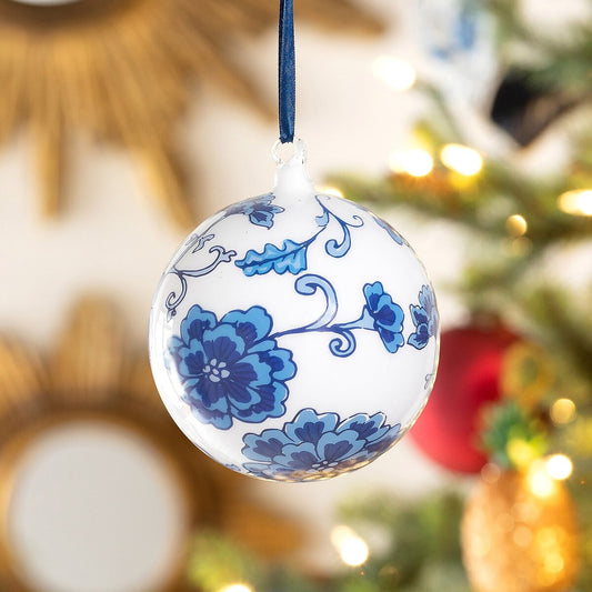 Decorative Christmas ball ornament with blue floral patterns hanging against a blurred festive background.
