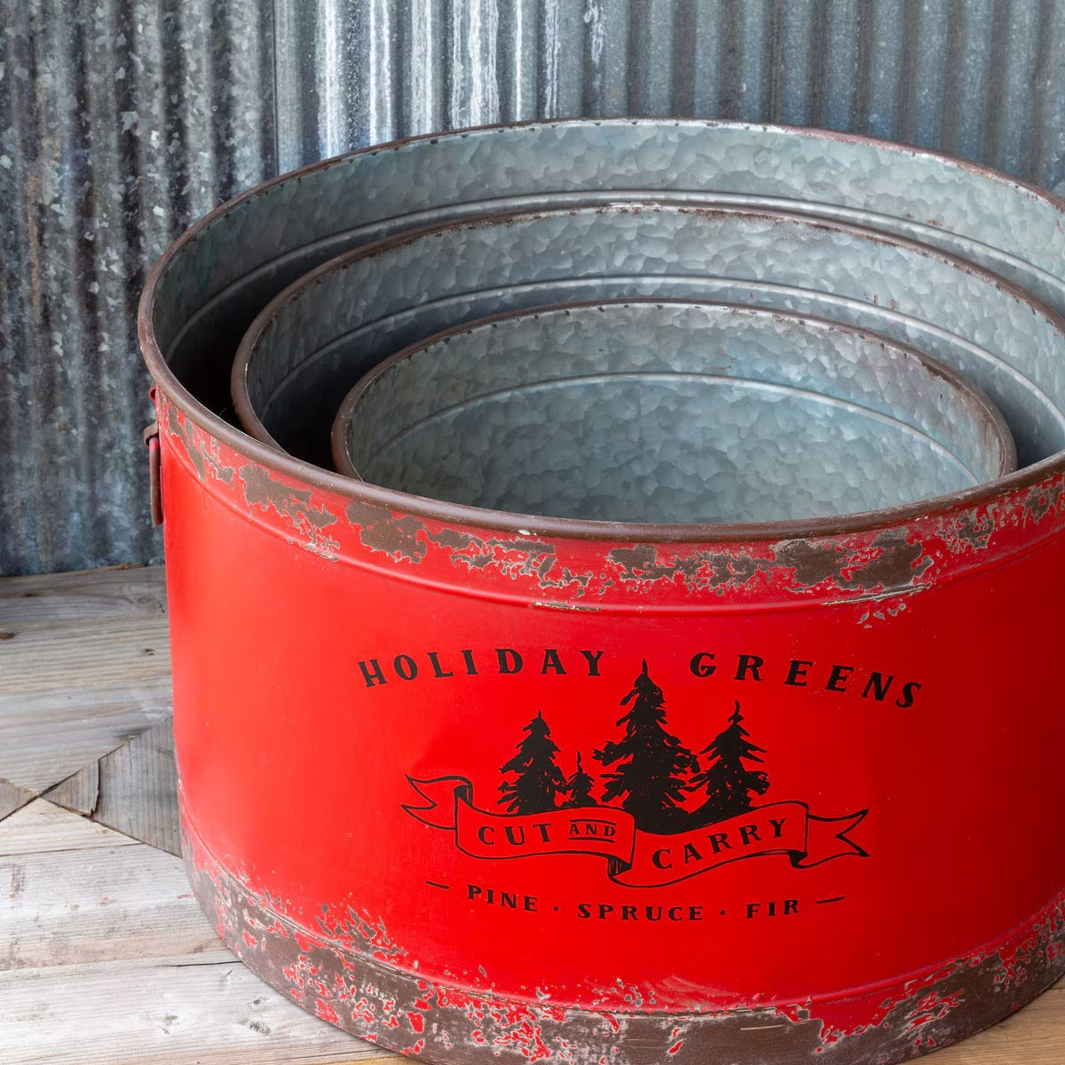 Red metal container with 'Holiday Greens' text and tree design against a corrugated metal background.