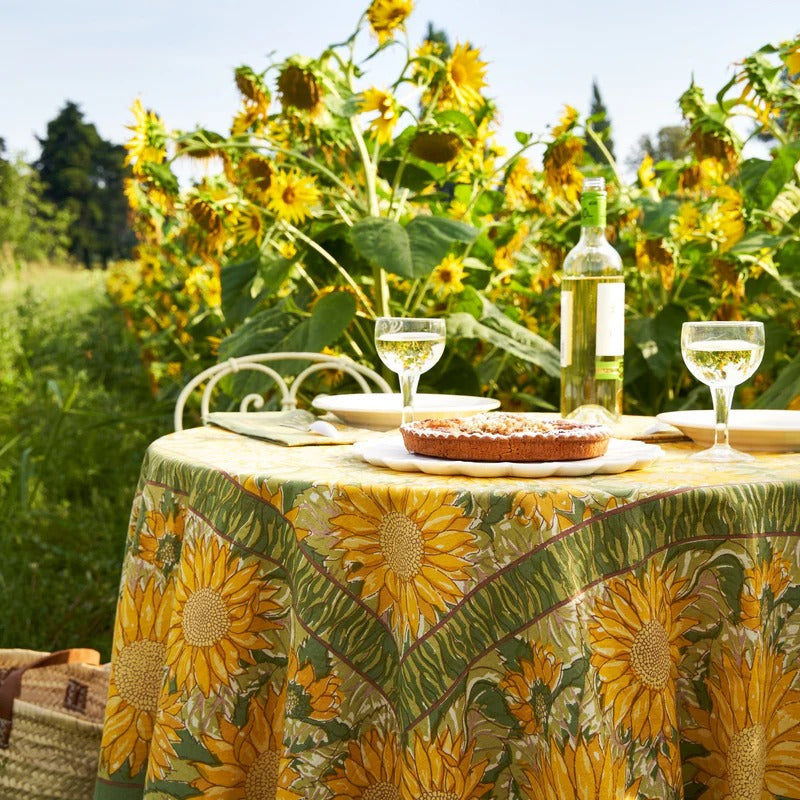 Table set with a sunflower-patterned tablecloth, pie, and wine glasses in a sunflower field.