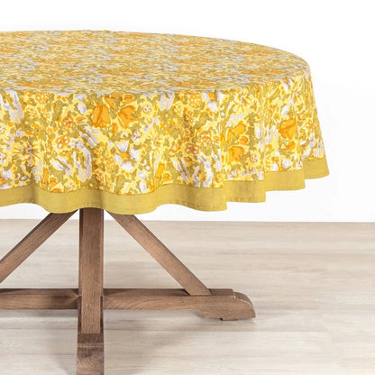 Round table with a yellow floral tablecloth on a wooden table.