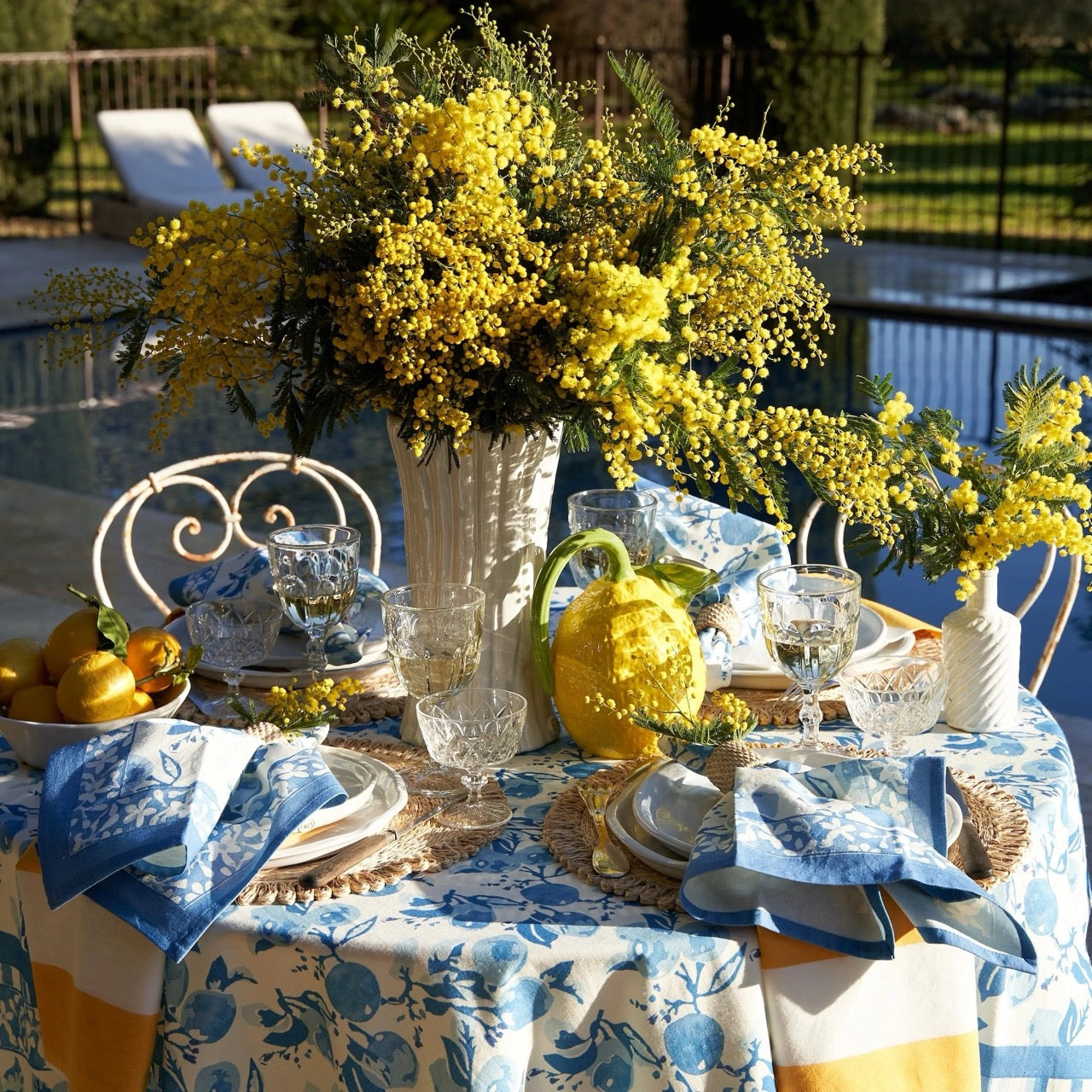 Decorative table setting with yellow flowers and blue and white tablecloth by a poolside.