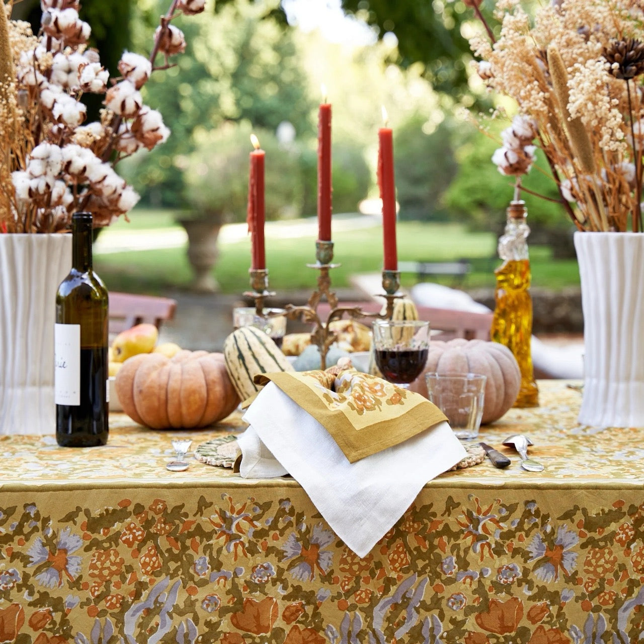 Decorative outdoor table setting with pumpkins, candles, and floral tablecloth.