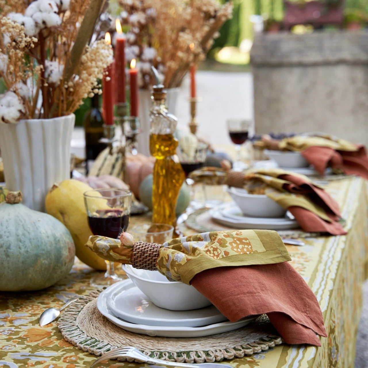 Decorative table setting with pumpkins, candles, and glasses on a tablecloth.