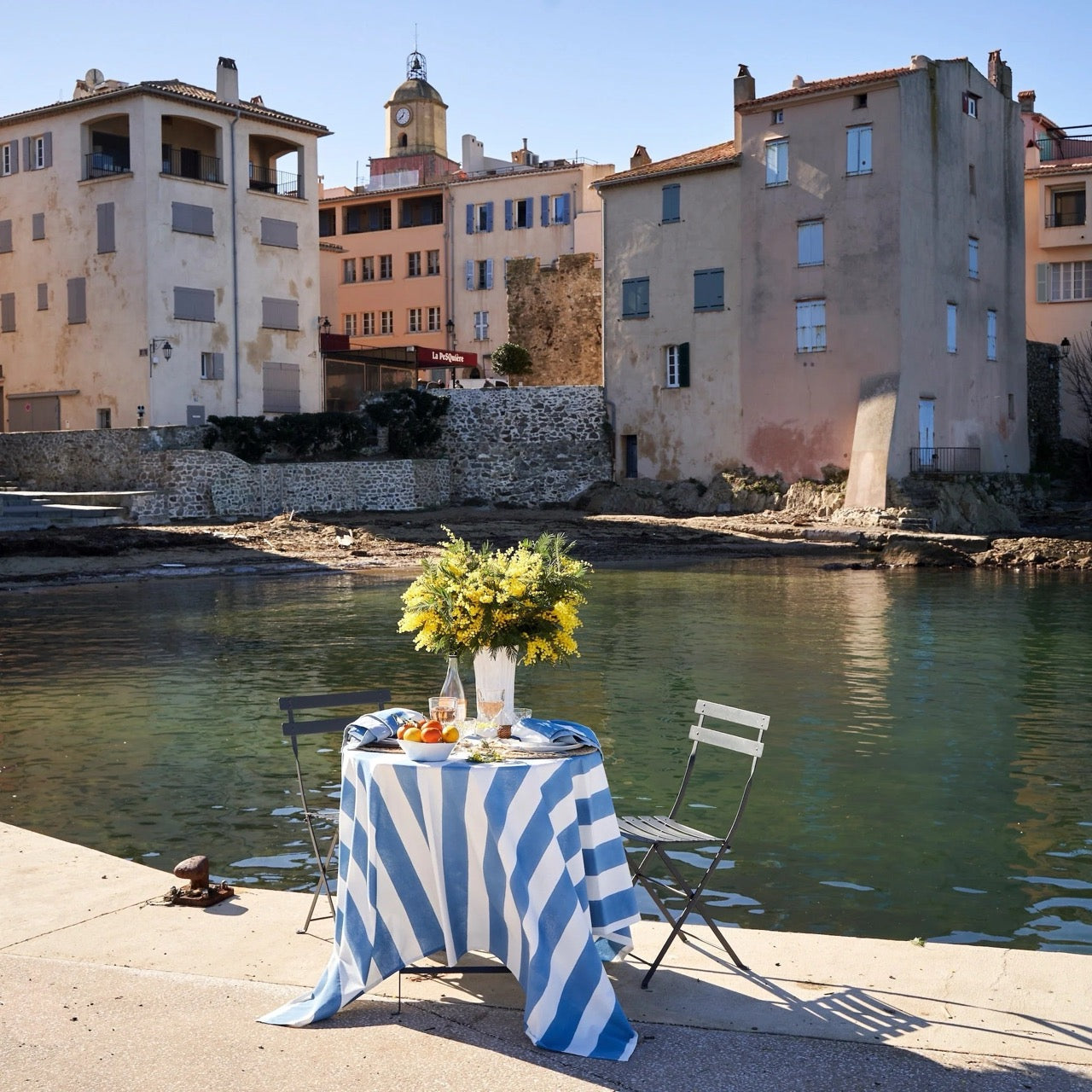 Table with a blue and white striped tablecloth by a waterfront with buildings in the background
