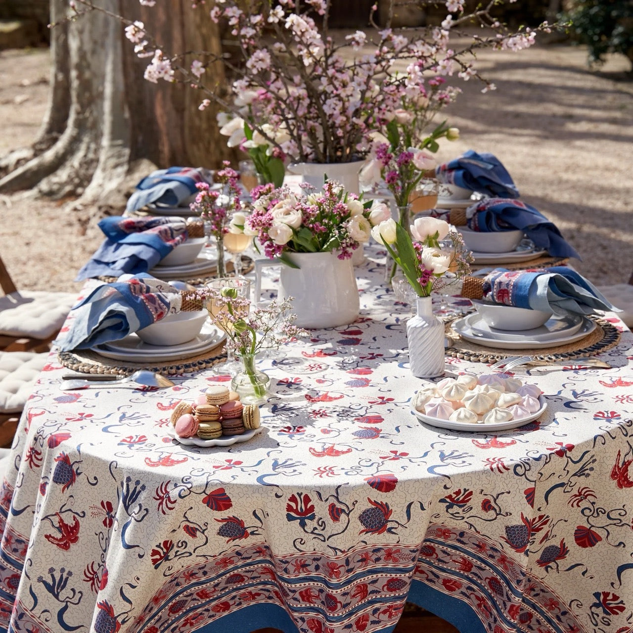 Decorative outdoor table setting with floral centerpieces and patterned tablecloth.