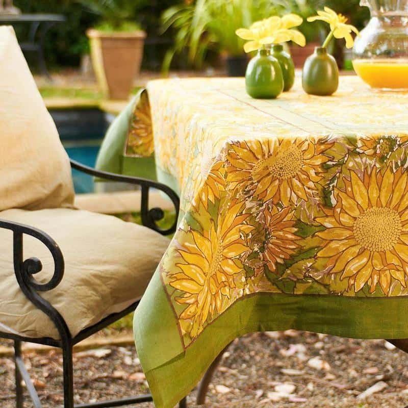 Outdoor setting with a tablecloth featuring sunflower design, chair, and potted plants.