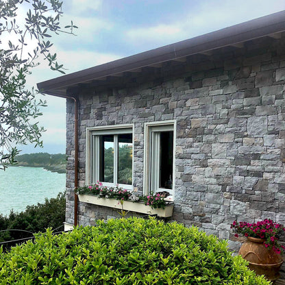Stone building with windows and flower boxes overlooking a body of water